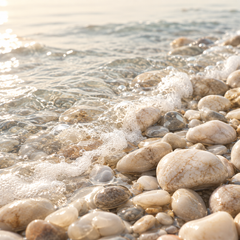Representative a close-up of clear shallow seawater gently washing over smooth pale coastal pebbles, subtle sea foam imagery for fragrance-note discovery