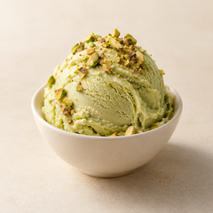 Representative one pale pistachio-green scoop of gelato in a small plain ivory bowl, sparse chopped pistachio garnish imagery for fragrance-note discovery